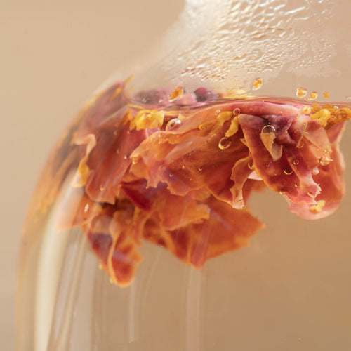 Close up of evening glow tea opening up while being brewed in a glass teapot 